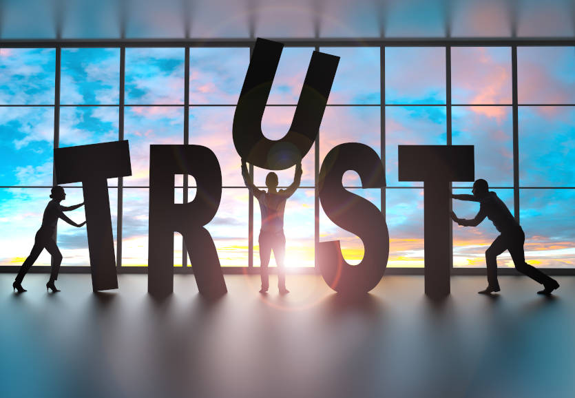 Larger than people sized letters spelling out the word trust. Three people positioning these letters working together as a team. 
