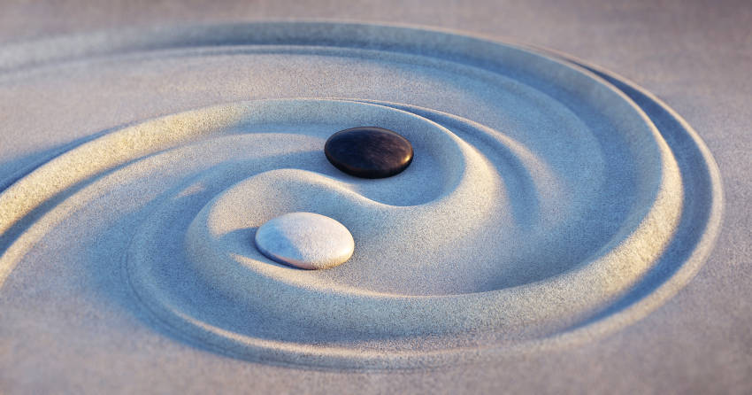 Two rocks, one black one white, in sand.  Two swirl lines drawn in sand, around the rocks.